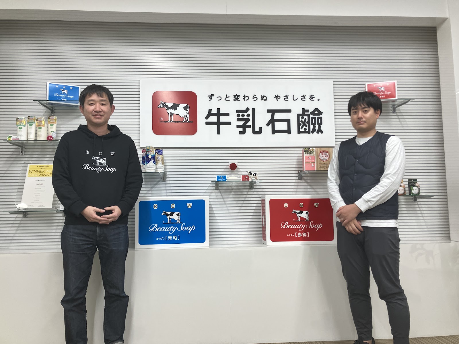牛乳石鹸の商品の前で並ぶ二人の男性の写真。