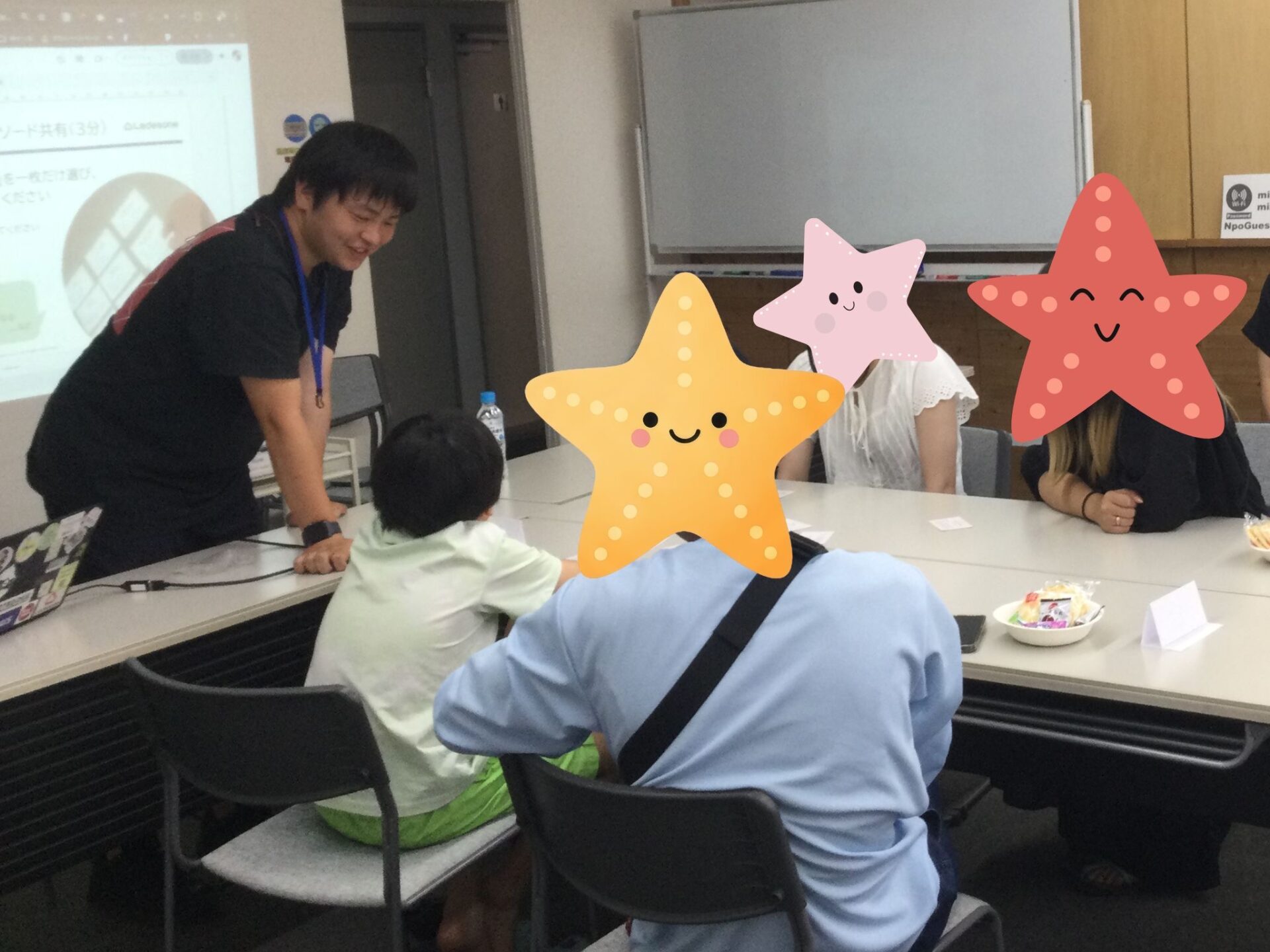 子ども数人がテーブルを囲み、が前に立って話している様子。スクリーンに資料が投影されている。